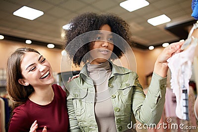 Two happy chic young mixed race woman shopping for lingerie in a clothing boutique with one holding panties as they Stock Photo