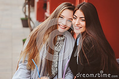 Two happy girl friends talking and drinking coffee in autumn city in cafe. Meeting of good friends, young fashionable students Stock Photo