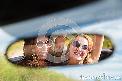 Two happy girls in a car rear-view mirror. Stock Photo