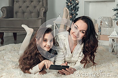 Two happy girls, mother and daughter lie on a floor in Christmas decorated room, use a mobile phone for access to Internet Stock Photo