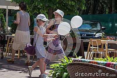 Two happy girls walking on street with baloons during children protection day Editorial Stock Photo