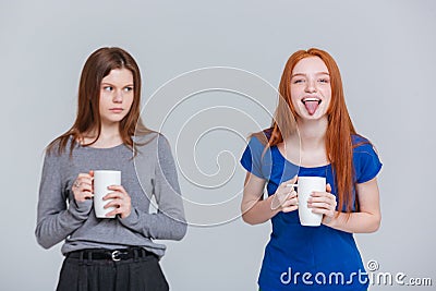 Two happy joking and sad frowning young women drinking tea Stock Photo