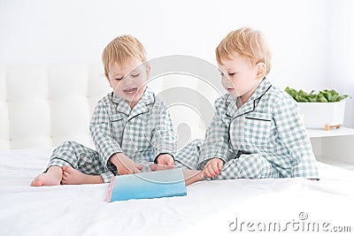 Two happy little boys brothers twins in pajamas reading book in their parents bed Stock Photo