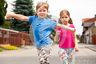 Two happy little children, sisters, siblings walking, girls jumping happily towards the camera with arms spread wide. Kids, family Stock Photo