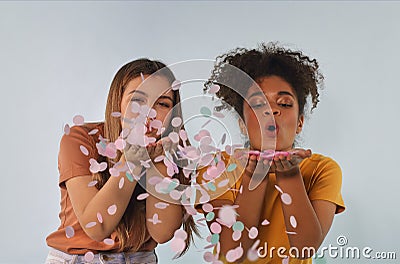 Two happy multiracial girlfriends blowing confetti at camera and having fun, enjoying birthday party Stock Photo