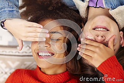 Two happy multiracial teen girls covering eyes and smiling while lying on blanket outdoors Stock Photo