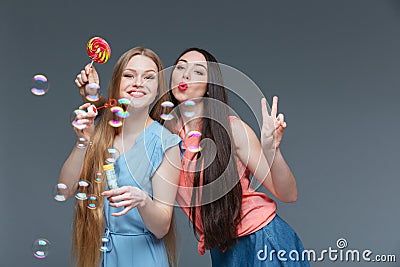 Two happy playful young women with colorful lollipop blowing bubbles Stock Photo