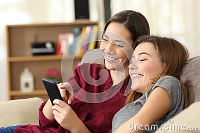 Two happy roommates checking smart phone content at home Stock Photo
