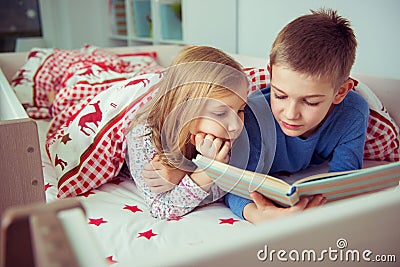 Two happy sibling children reading book in bunk bed under blanket Stock Photo