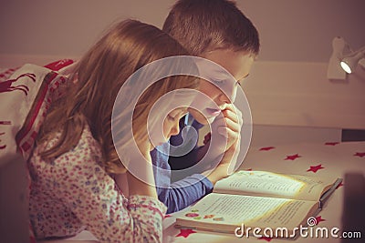 Two happy sibling children reading book in bunk bed under blanket Stock Photo