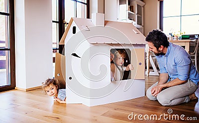 Two toddler children with father playing with paper house indoors at home. Stock Photo