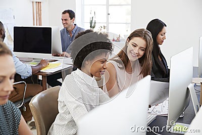 Two happy women discuss work at computer in open plan office Stock Photo