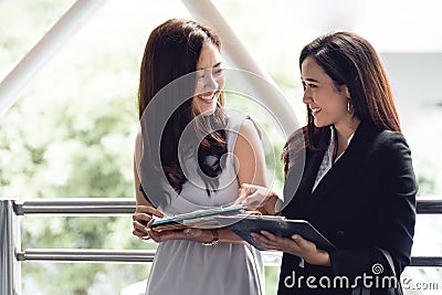 Two happy young Asian businesswomen looking into document file folder for analyzing profit or sale break even point after Stock Photo