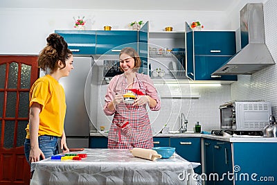 Two happy young Caucasian women cook together in the kitchen. The concept of LGBT couples and family cooking Stock Photo