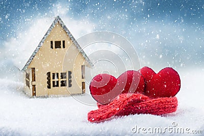 Two hearts wrapped in a warm scarf in the snow near the house during a snowfall Stock Photo