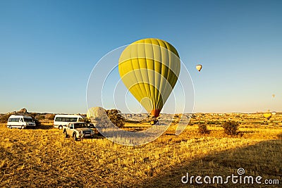Two hot-air balloons taking off or landing in a field. One is on the ground. The other is airborne with crew member in vehicle Editorial Stock Photo