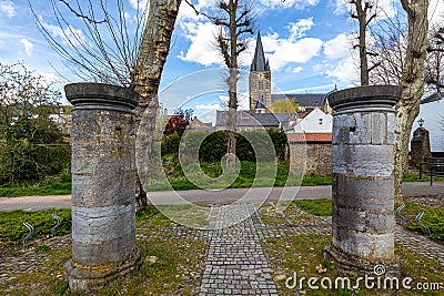 Two huge thick pillars with a pedestrian path, houses and bell tower of St. Michael Abbey churc Stock Photo