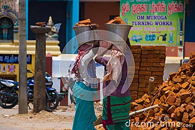 Two Indian women carry heavy bricks on their heads in traditional clothes. View from the back. Use of female labor at Editorial Stock Photo