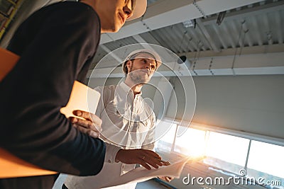 Two industrial engineers wearing safety hard hat have meeting on commercial building structure Stock Photo