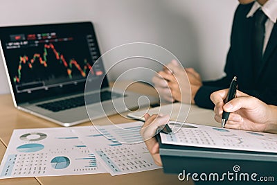 Two investors are working together with analyzing the stock data graphs in the paper and viewing the data on the laptop screen Stock Photo