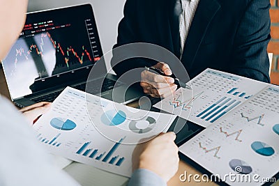 Two investors are working together with analyzing the stock data graphs in the paper and viewing the data on the laptop screen Stock Photo