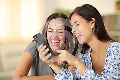 Two joyful roommates laughing watching media on phone Stock Photo