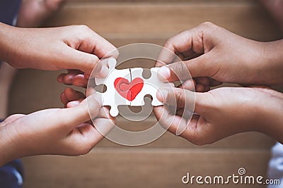 Two kid hands connecting couple jigsaw puzzle with drawn red heart Stock Photo