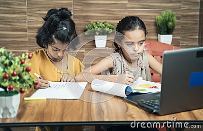 Two kids busy in writing by looking into the laptop during online or virtual class at home - concept of e-learning or distance Stock Photo