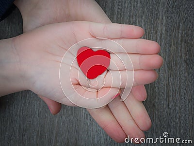 Two kids holding red heart in hand over solid wooden background Stock Photo