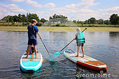 Two Kids Outside on Lake Learning to Stand Up Paddle Board on Summer Day Stock Photo