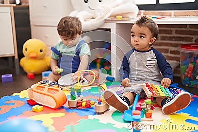 Two kids playing xylophone and tambourine sitting on floor at kindergarten Stock Photo