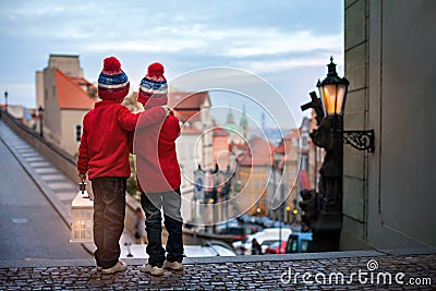 Two kids, standing on a stairs, holding a lantern, view of Prague behind them, snowy evening Stock Photo