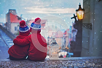 Two kids, standing on a stairs, holding a lantern, view of Prague behind them, snowy evening Stock Photo