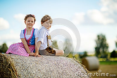 Two kids, boy and girl in traditional Bavarian costumes in wheat field with hay bales Stock Photo