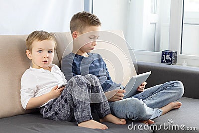 Two kids using gadgets at home. Brothers with tablet computer in light room. Boys playing games on tablet pc, emotions. Stock Photo