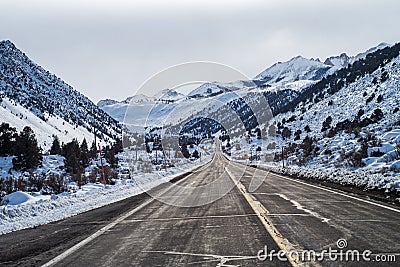 Two lane paved road ascending into snowy mountains Stock Photo