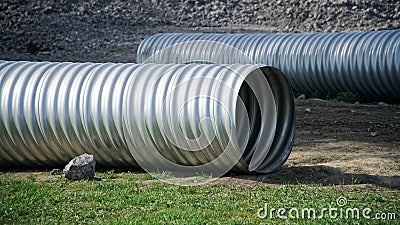 Two large corrugated metal pipes, prepared for installation, lie on a construction site next to a pile of gravel and green grass. Stock Photo