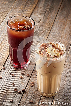 Two large tall glasses with cold coffee sprinkled with almonds and chocolate on wooden table. Coffee beans are scattered Stock Photo