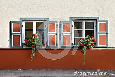 Two lattice windows with red and grey painted shutters, flower pot with geranium, concrete facade Stock Photo