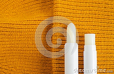 Two lip balms on the orange knitted background. Winter lip care sticks with beeswax, honey, panthenol and shea butter. Copy space. Stock Photo