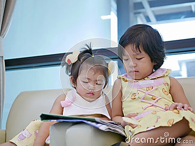 Two little Asian baby girl, sisters, sitting and watching a smartphone together, while waiting for her mother Stock Photo