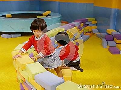 Two little Asian baby girls, sisters, stacking up foam building bricks / blocks together at an indoor playground Stock Photo