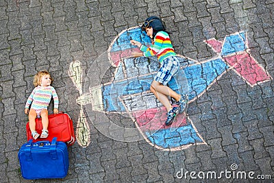 Two little children, kid boy and toddler girl having fun with with airplane picture drawing with colorful chalks on Stock Photo