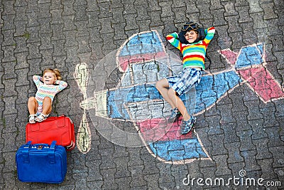 Two little children, kid boy and toddler girl having fun with with airplane picture drawing with colorful chalks on Stock Photo