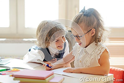 Two little classmate, laddie and girlie, are sitting at the same desk. Stock Photo