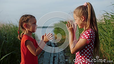 Two little cute girls playing patty cake game, having fun by the lake. Two little cute girls playing patty cake game, having fun on wooden boards by the lake stock footage Two little cute girls playing patty cake game, having fun by the lake. Two little cute girls playing patty cake game, having fun on wooden boards by the lake stock footage