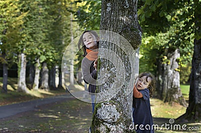 Two little girl looking from behind a tree Stock Photo