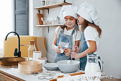 Two little girls in blue chef uniform talking secrets to each other when preparing food on the kitchen Stock Photo