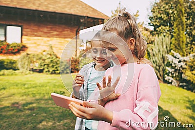 Two little girls outside their house are talking on a mobile phone with friends or parents via video link. Stock Photo