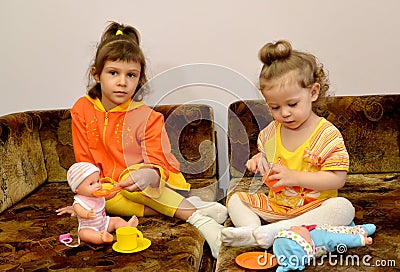 Two little girls play with dolls on a sofa Stock Photo
